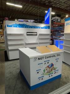 RENTAL: Custom Island Design with Conference/Storage Room with White Laminated Product Shelves, 12 Ft. High Double-Sided Lightbox, RE-1567 Backlit Reception Counter, RE-1572 L-Shape Backlit Counter, (2) Large Monitor Mounts, Double-Sided Kiosk with RE-120
