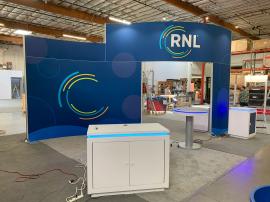 RENTAL: RE-9135 Island Rental Design with 16’ High Curved Gravitee Panel System Structure with (1) RE-1576 White Laminated Reception Counter, (2) RE-1575 White Laminated Workstation Counters, (4) Large Monitor Mounts, (8) LED Arm Lights, SEG Fabric Grap